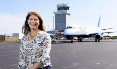 凯特·塞维斯站在机场停机坪上，身后是一架喷气式飞机和控制塔.